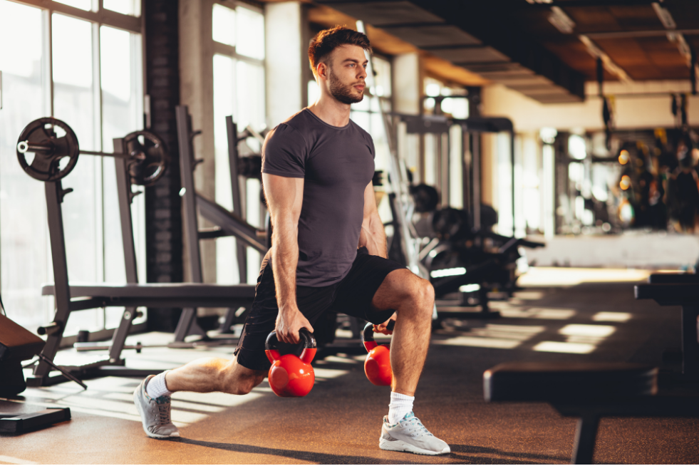 Man in the gym holding kettlebells in a lunge position 