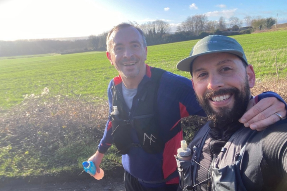 Pete and his colleague Jay in running kit posing for a selfie, with a green field in the background