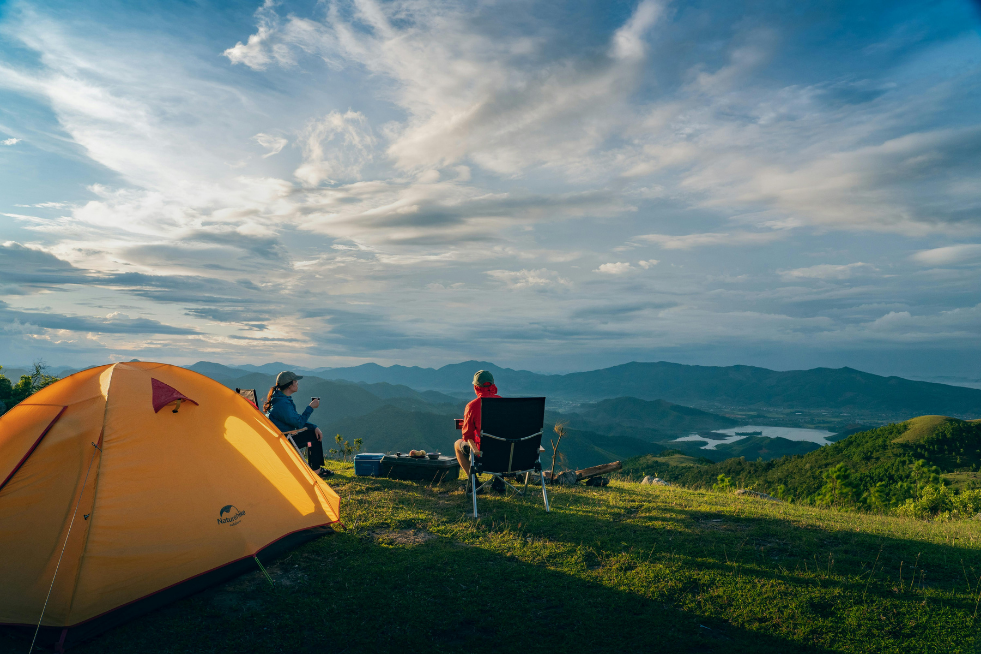 Two campers outside a tent on a hillside