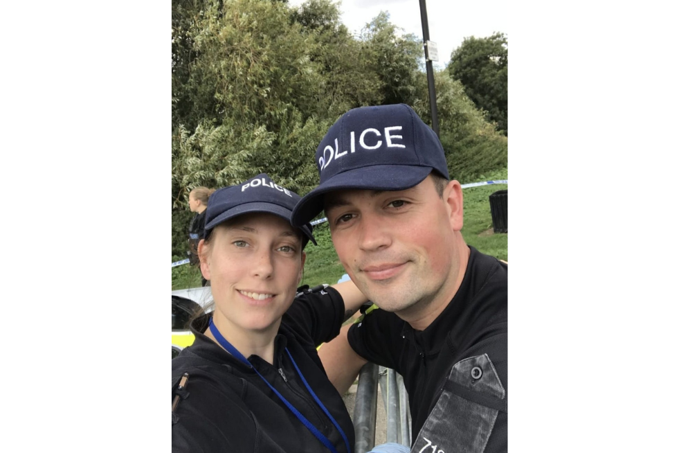 A male and female police officer posing for a selfie, both wearing Police caps