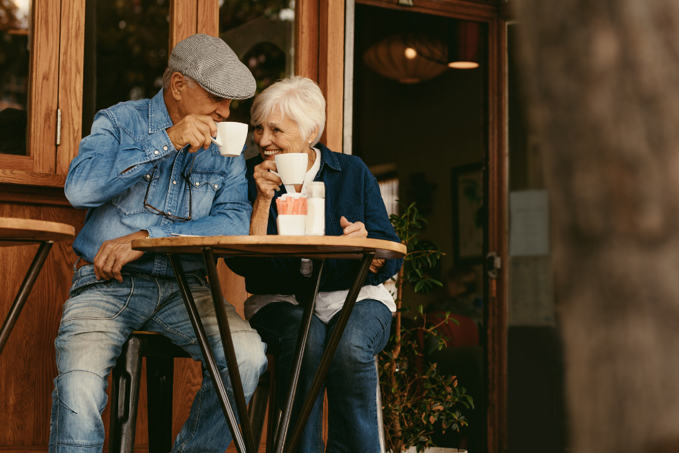 An elderly couple sat outside having a hot drink