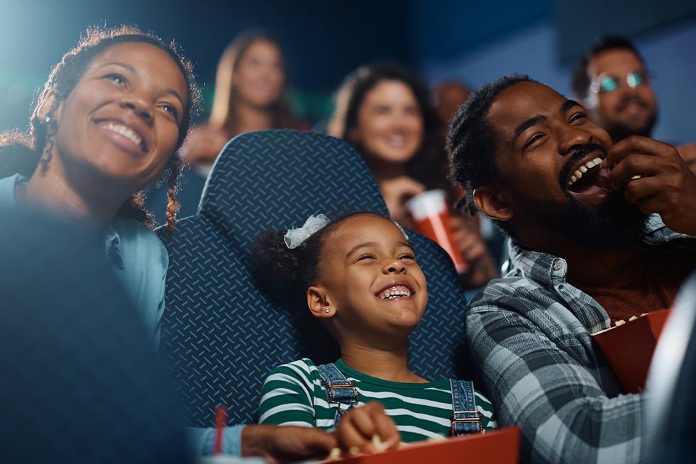 A family of three at the cinema smiling and eating popcorn