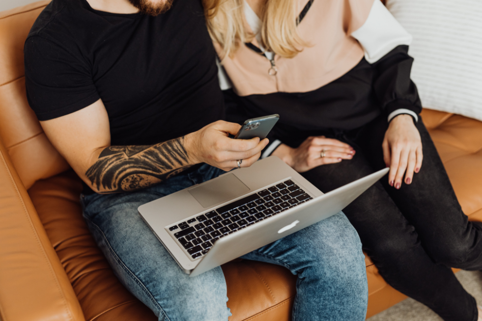 A couple sitting on a sofa with a laptop and a phone