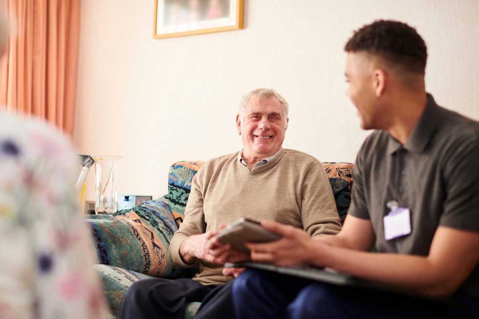 An elderly man sat on a sofa speaking with a young man 