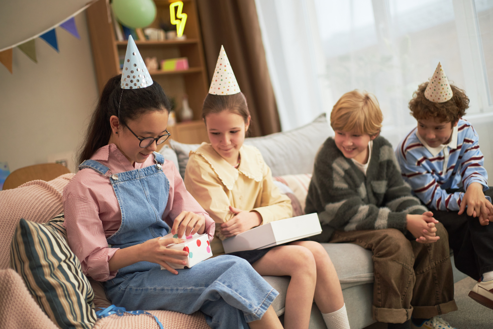 A group of kids watching a girl open her birthday presents 