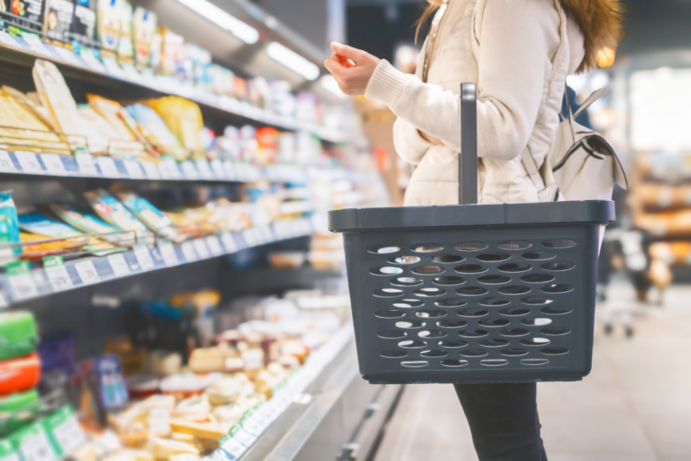 A woman with a shopping basket standing in front of produce at the supermarket