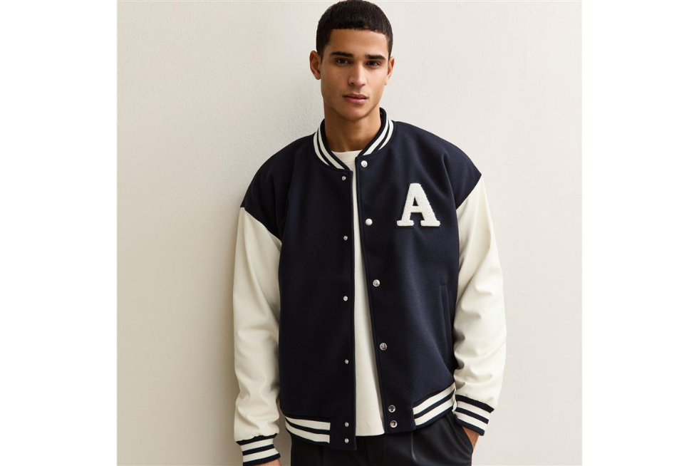 A man wearing a navy blue and white varsity jacket from New Look