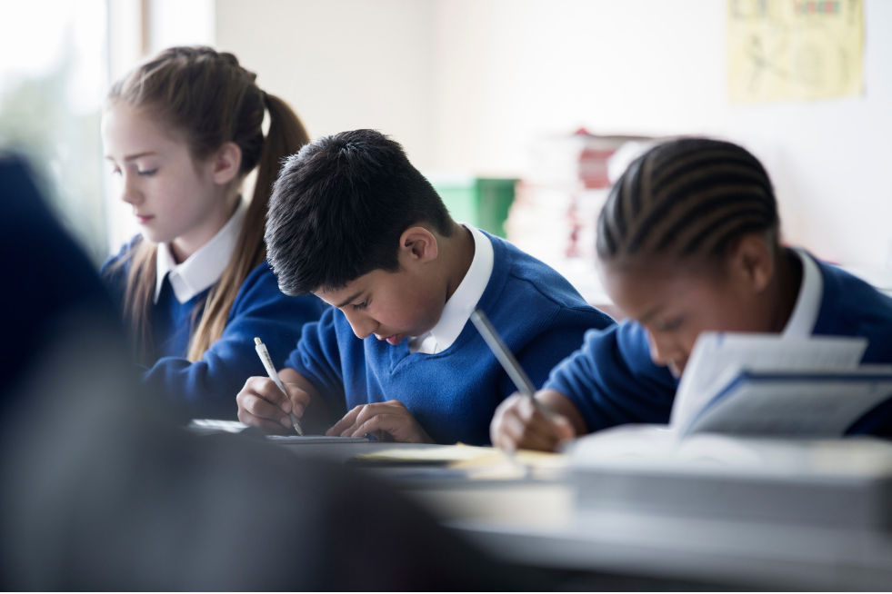 Three children in a classroom writing