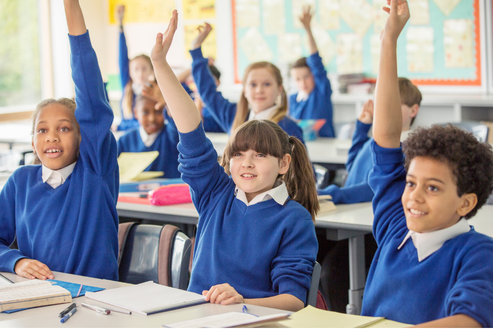 School children in a classroom with their hands up