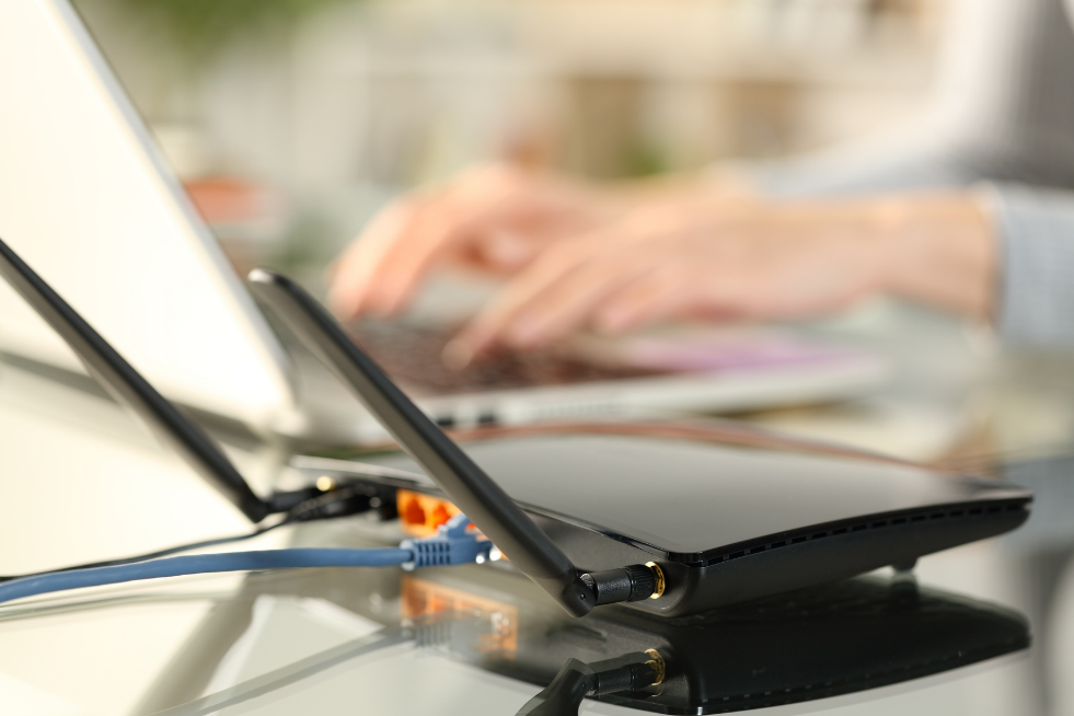A wi-fi router next to someone typing on a laptop