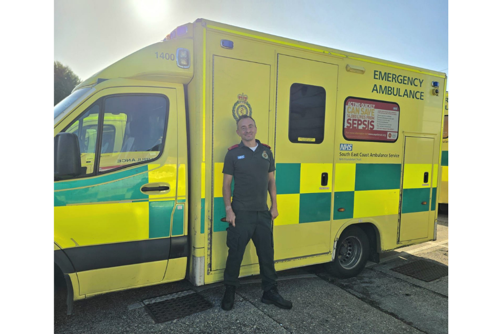 A paramedic standing smiling in front of an ambulance