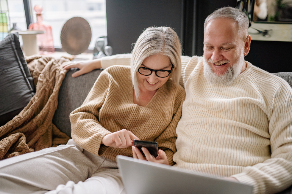 A couple on the sofa at home looking at a phone and laptop