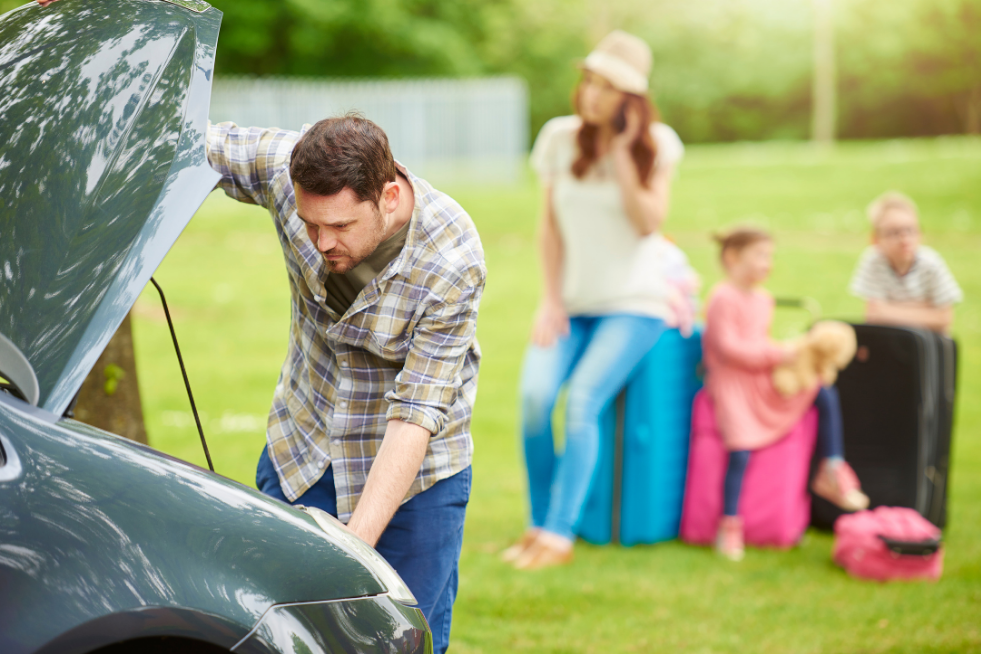 A man looking under the bonnet and his family sat with suitcases