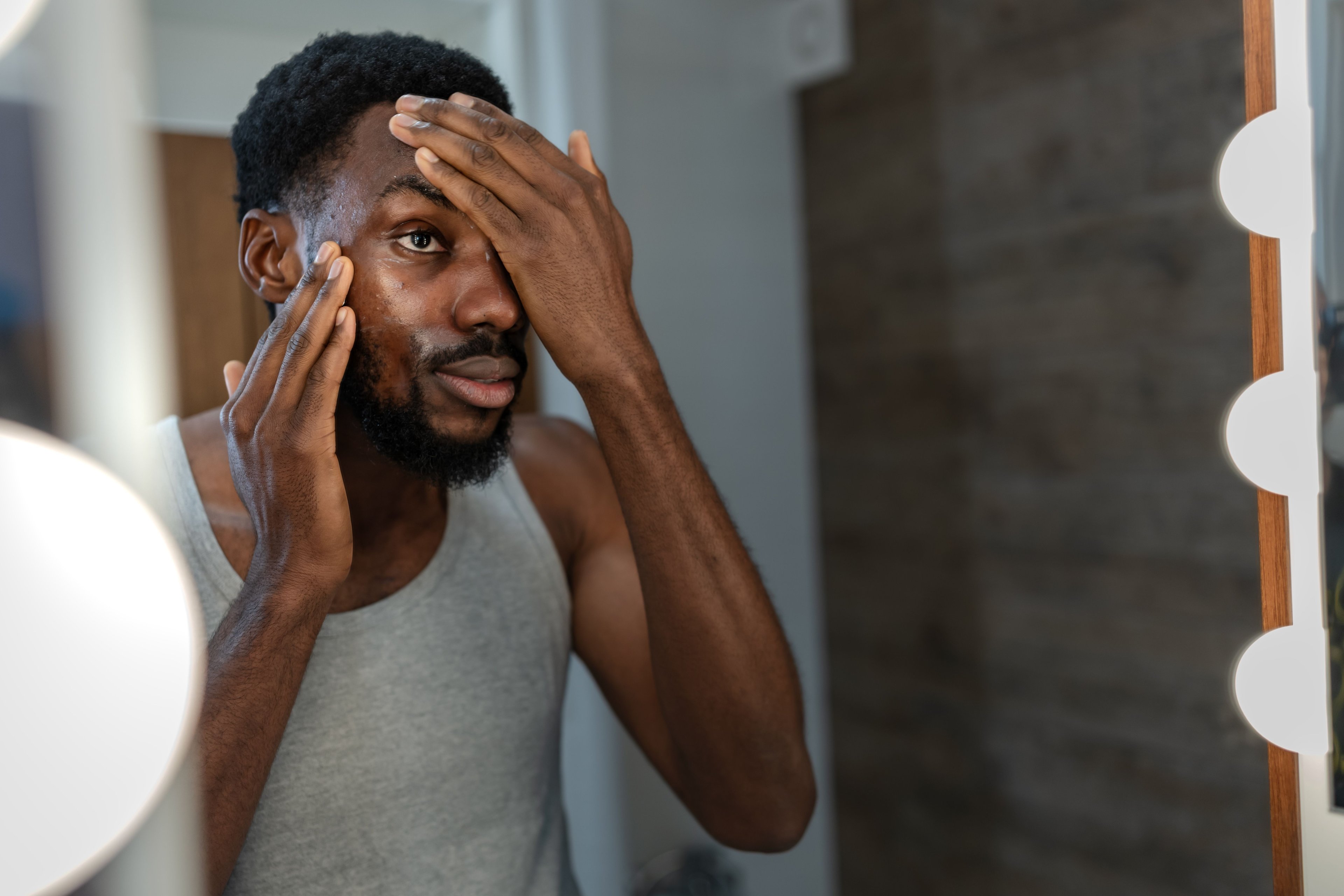 A man looking in the mirror and applying lotion to his face